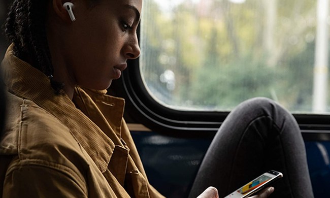A woman wears AirPods Pro while looking at her iPhone on public transportation.