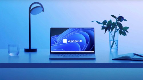 A laptop sits on a desk with a Windows 11 wallpaper.