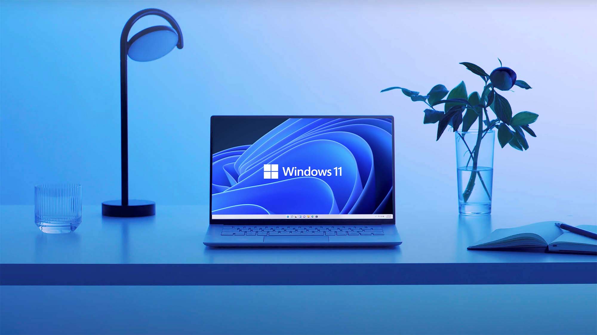 Una computadora portátil se encuentra en un escritorio con un fondo de pantalla de Windows 11.