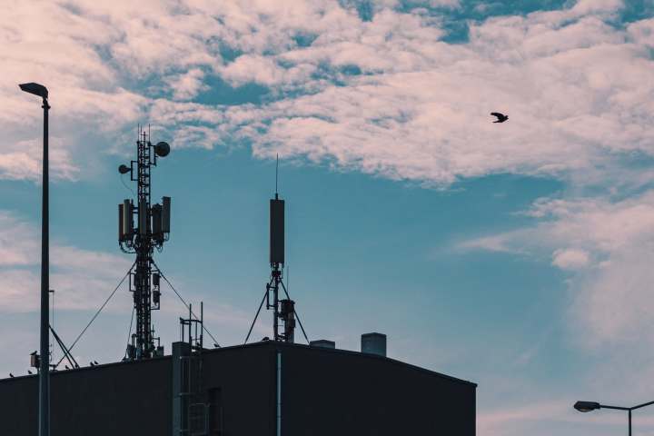Cellular radio towers on roof of building against sky with clouds.