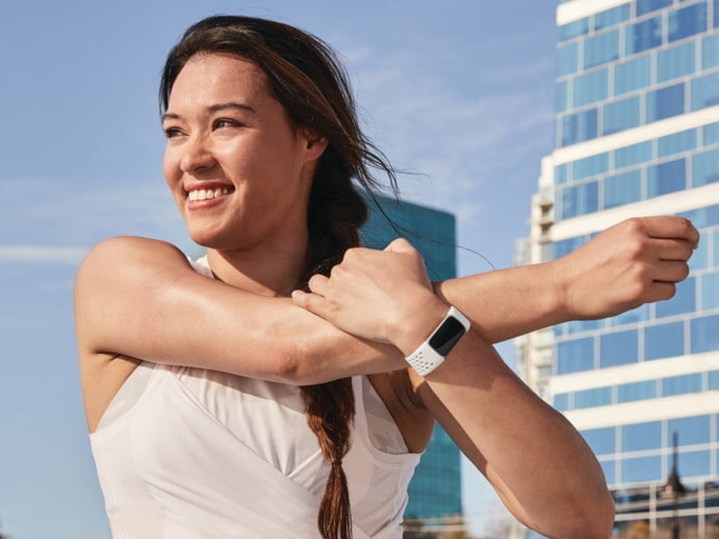 زنی که Fitbit Charge 5 پوشیده است، شانه خود را در حین ورزش دراز می کند.