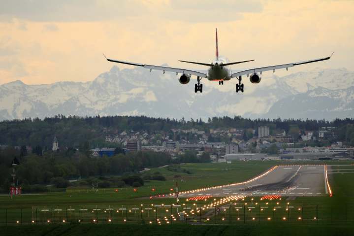 Aviones que aterrizan al atardecer sobre una pista con los Alpes suizos al fondo.
