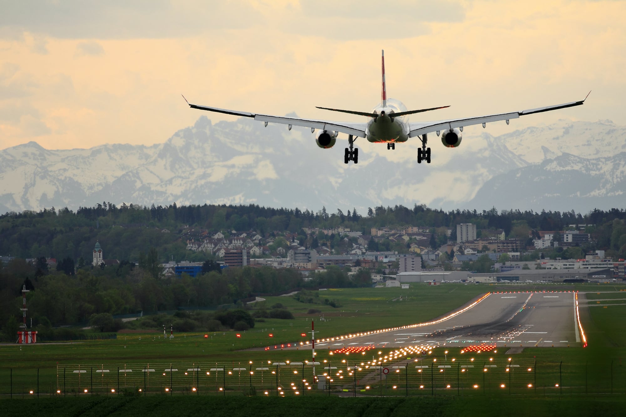 Aviones que aterrizan al anochecer sobre una pista con los Alpes Suizos al fondo.