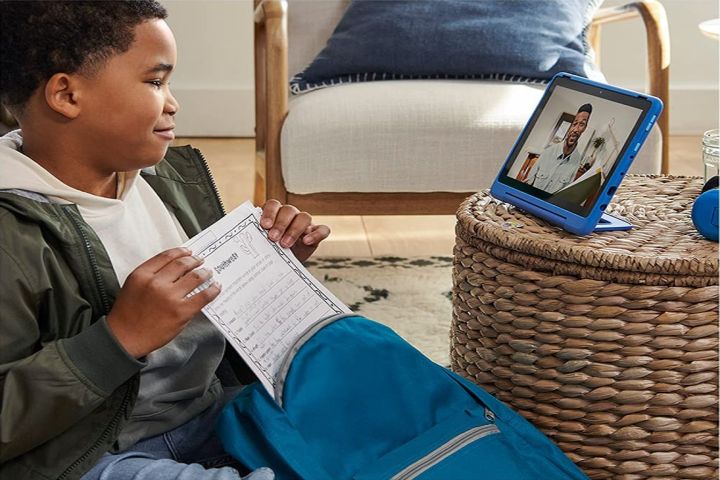 A little boy with a worksheet watching video on a blue Amazon Fire HD 10 Kids Pro tablet.
