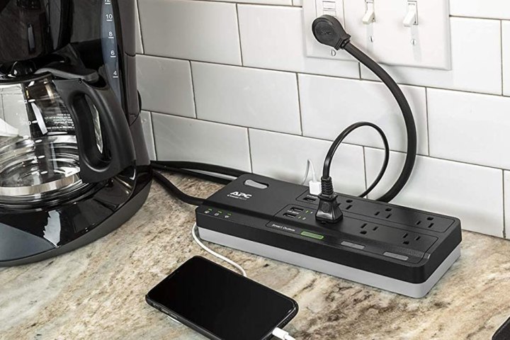 APC surge protector on kitchen counter charging iPhone and powering coffee machine.