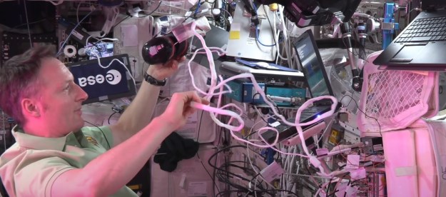 An astronaut tries to untangle the wire on a pair of headphones.