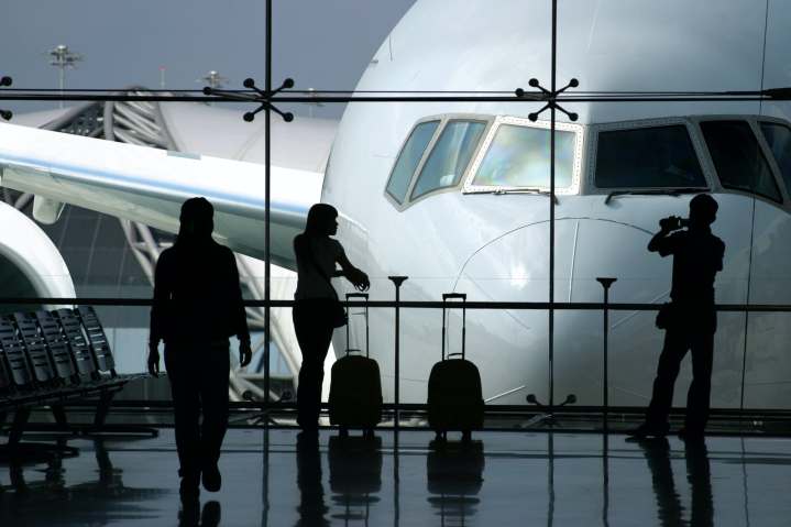 Three silhouetted passengers in airport waiting area with large airliner in background.