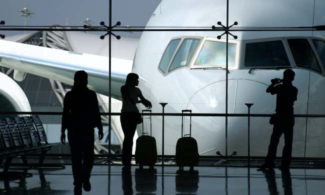 Three silhouetted passengers in airport waiting area with large airliner in background.