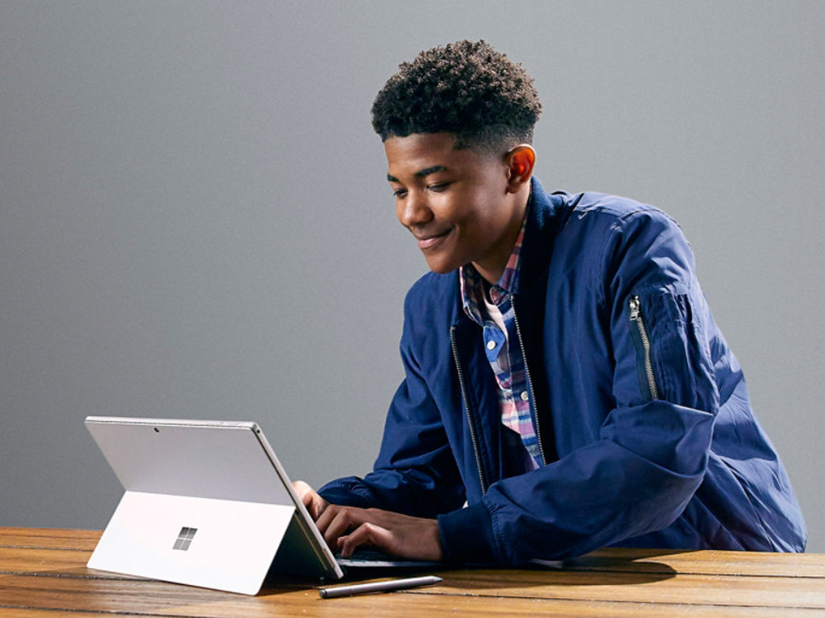 学生在配有专业键盘盖的桌子上使用 Microsoft Surface Pro 7。