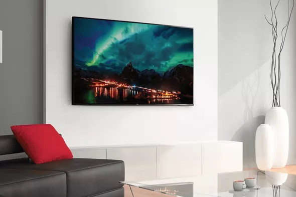 A TCL 65-inch Class 4-Series 4K TV mounted on a living room wall with an image of the Northern Lights on screen.