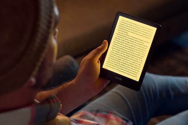 A person sits while reading on an Amazon Kindle Paperwhite.