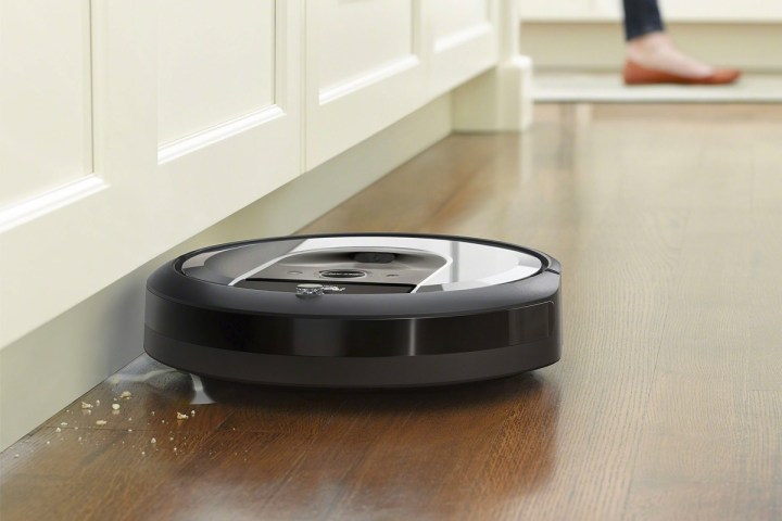 iRobot Roomba i6 (6150) Wi-Fi Connected Robot Vacuum - Light Silver on a hard wood floor sucking up dirt.