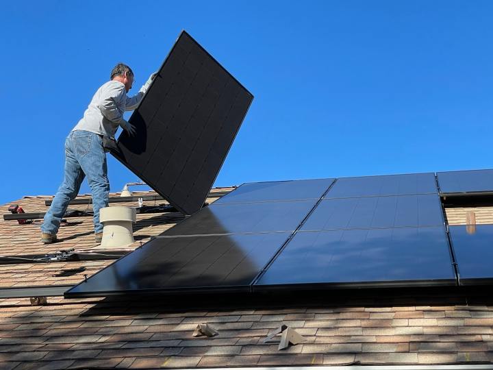Мужчина устанавливает солнечную панель на крыше дома.