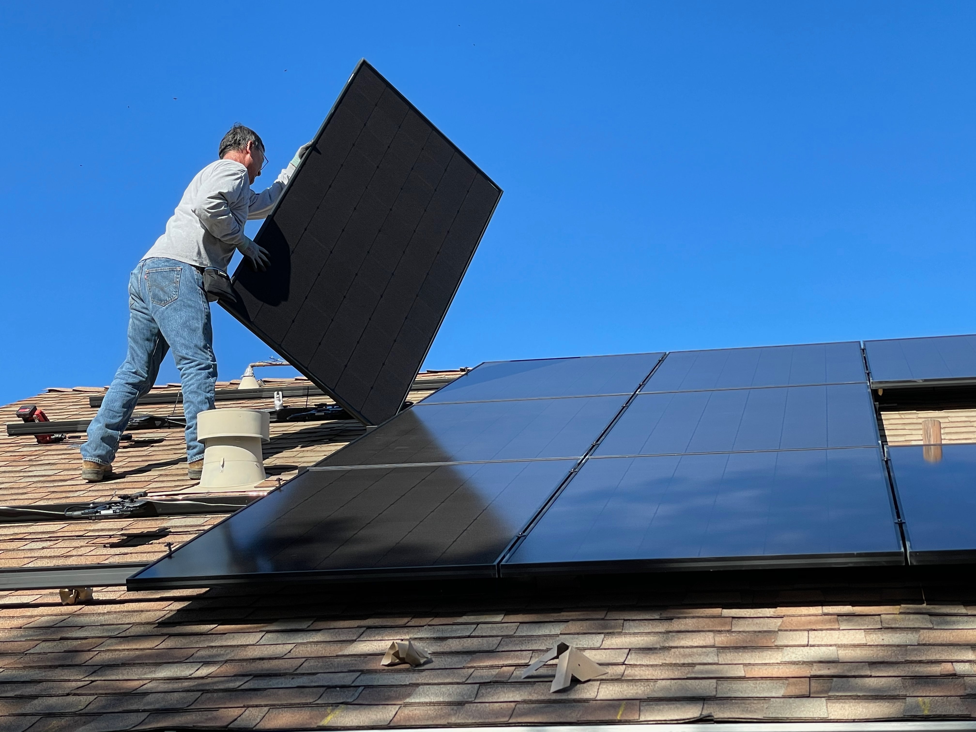 Un hombre instalando un panel solar en el techo de una casa.