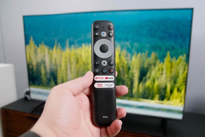 The TCL 6-series Google TV's remote being held up in front of the TV.