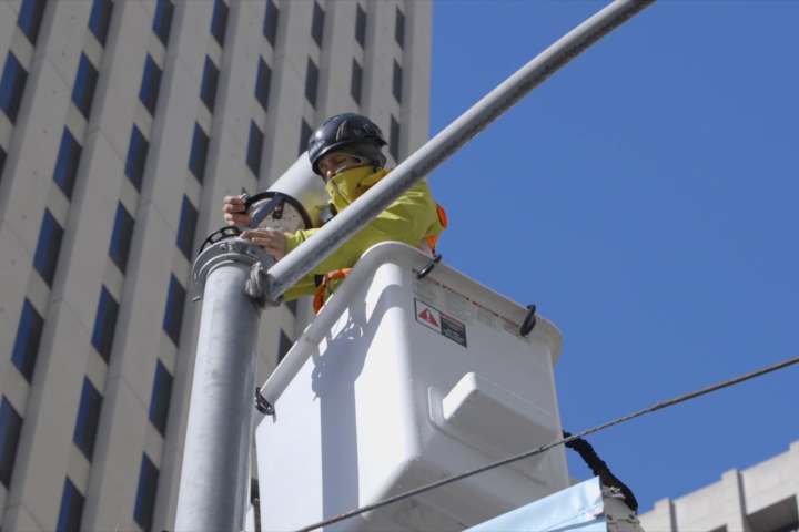 Worker in crane basket installing 5G antenna on building.