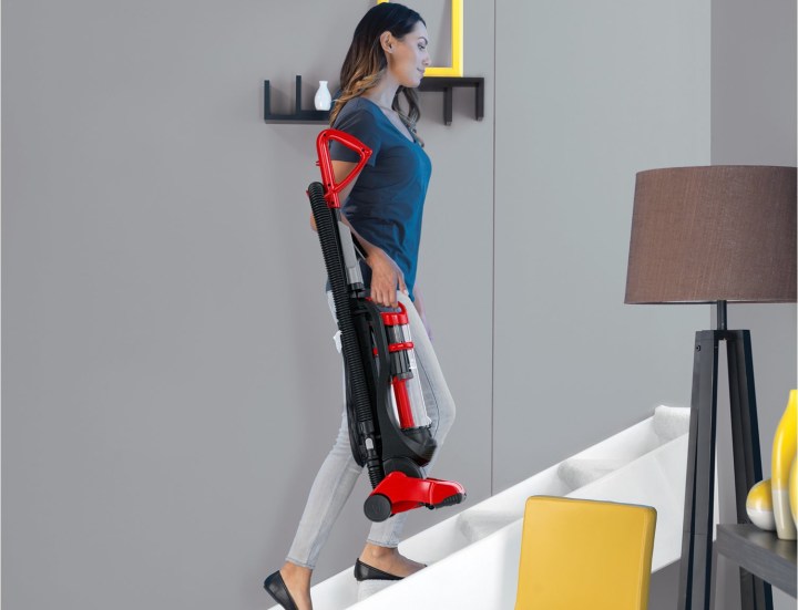 Woman carrying Dirt Devil Power Express Upright Bagless Vacuum up stairs.