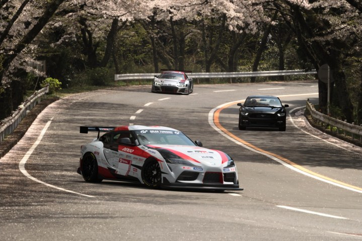 Three cars come racing around a tight turn in Gran Turismo 7.