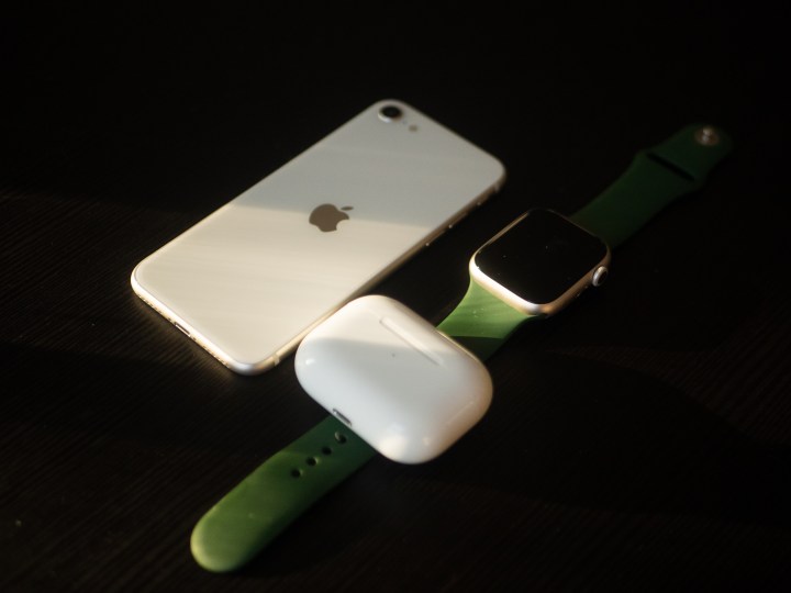 An iPhone SE 2022 sitting on a table with an Apple Watch and AirPods Pro.