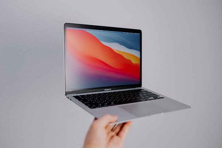 A person holding a MacBook Air against a gray background.