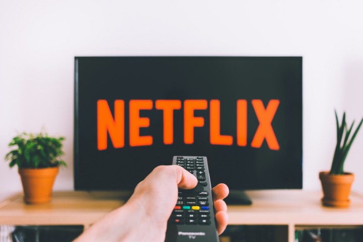 A hand points a remote at a TV display a Netflix logo screen.