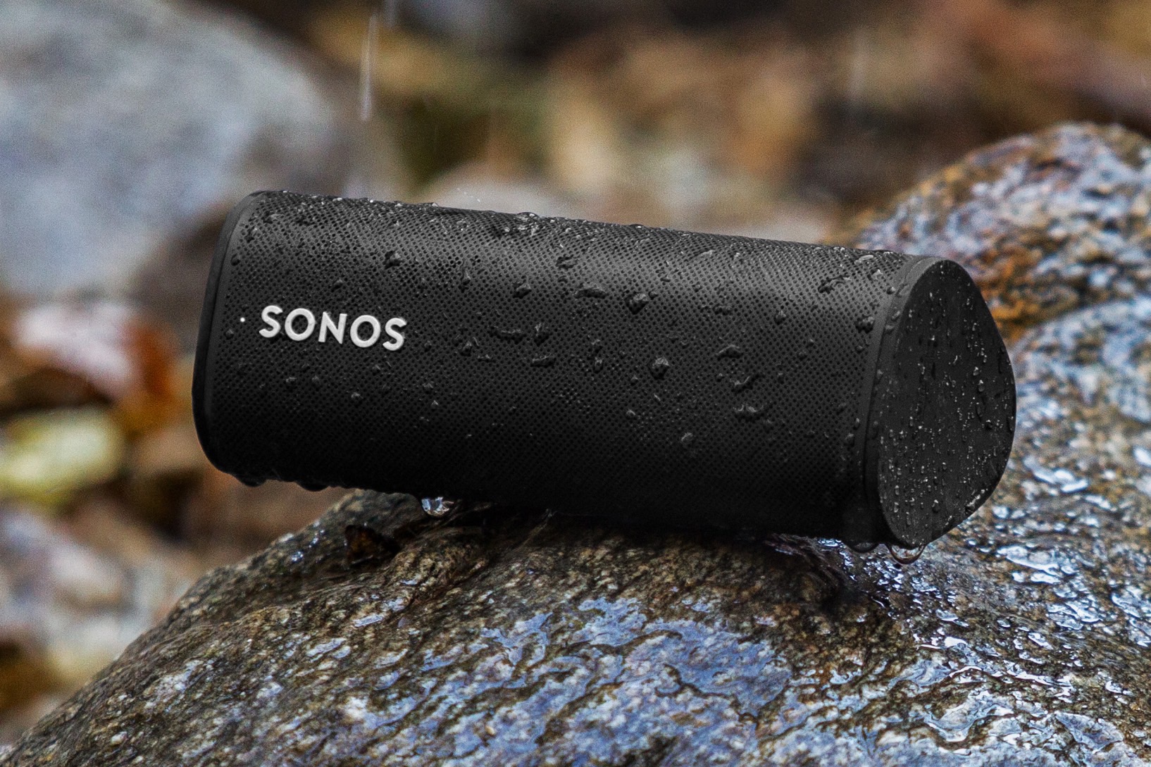 Sonos Roam SL em preto em uma rocha chuvosa ao ar livre.