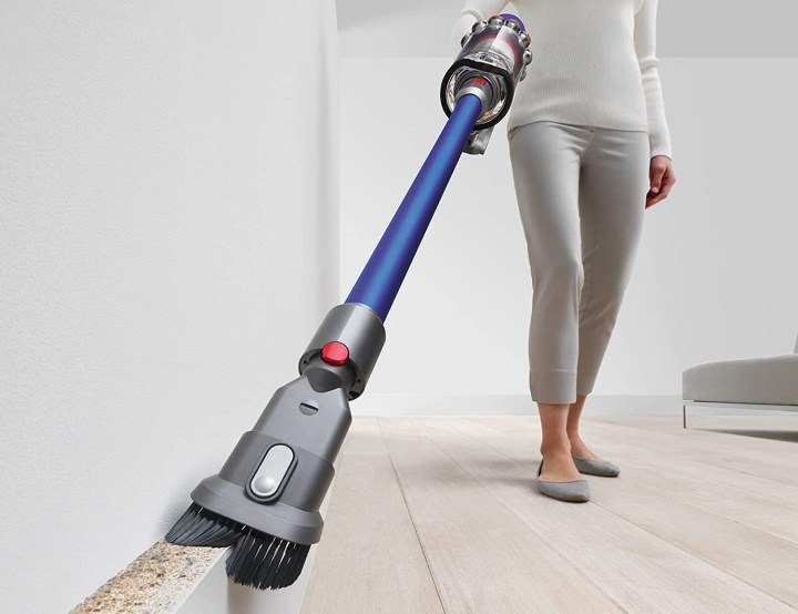 Woman vacuuming dusty baseboards with a Dyson V10 Allergy Cordless Stick Vacuum Cleaner.