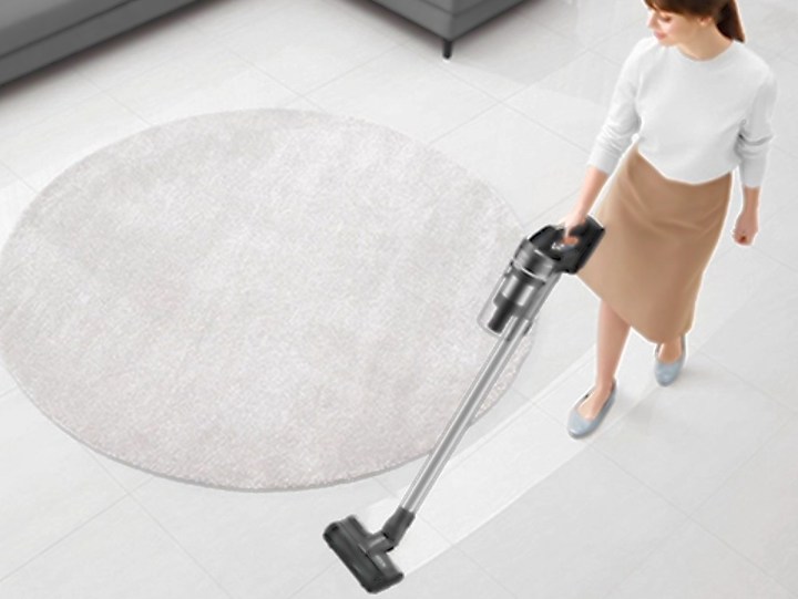Woman vacuuming living room carget with Samsung Jet 75 Complete Cordless Stick Vacuum.