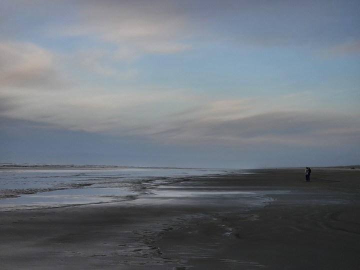 Una spiaggia al tramonto con due persone lontane.