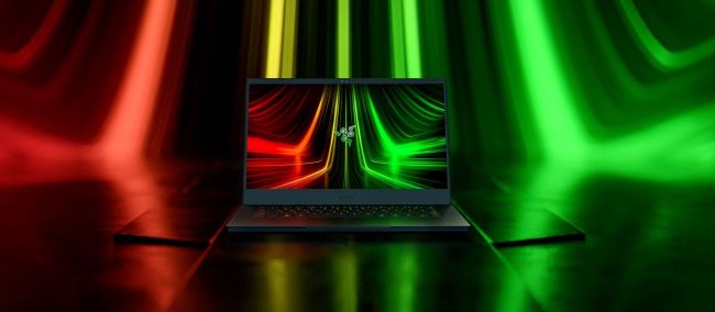 The Razer Blade 14 gaming laptop sits on a reflective floor surrounded by red and green streaks of light.