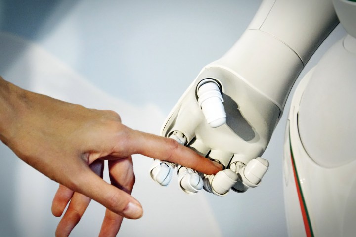 A woman's hand is held by a robot's hand.