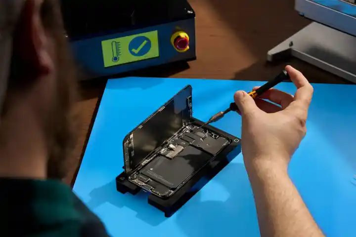 Person fixing an open iPhone with tool on a blue table.