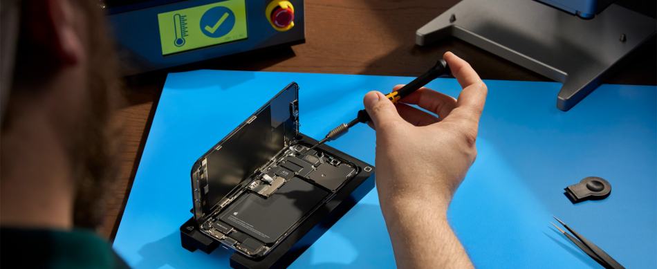 Person fixing an open iPhone with tool on a blue table.