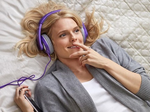 A woman wearing headphones and lying on a bed listens to an Audible audio book.