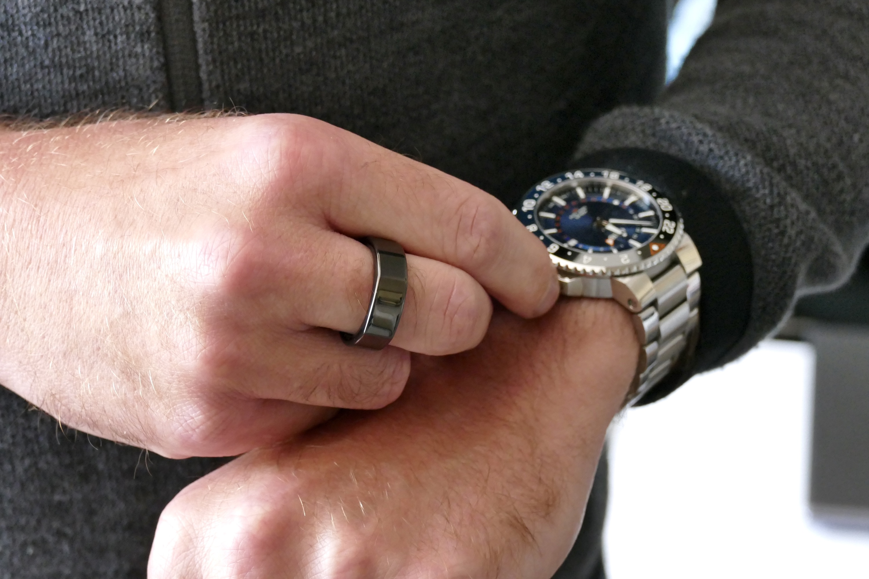 The Oura Ring worn on a man's finger, when winding a watch.