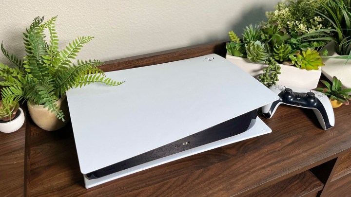 A standard white PS5 sitting near some small plants in a home entertainment center.