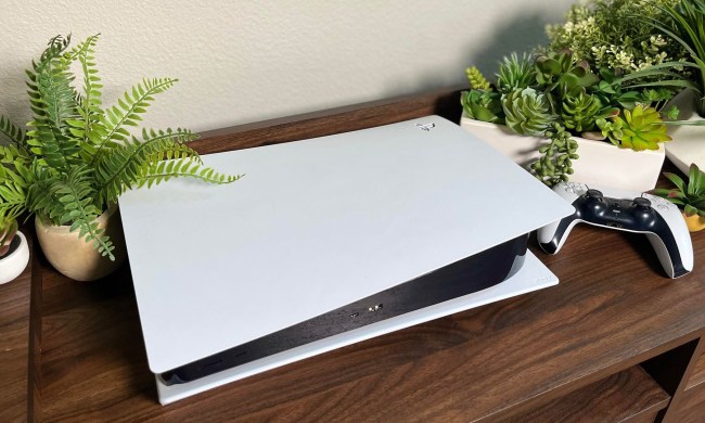 A standard white PS5 sitting near some small plants in a home entertainment center.