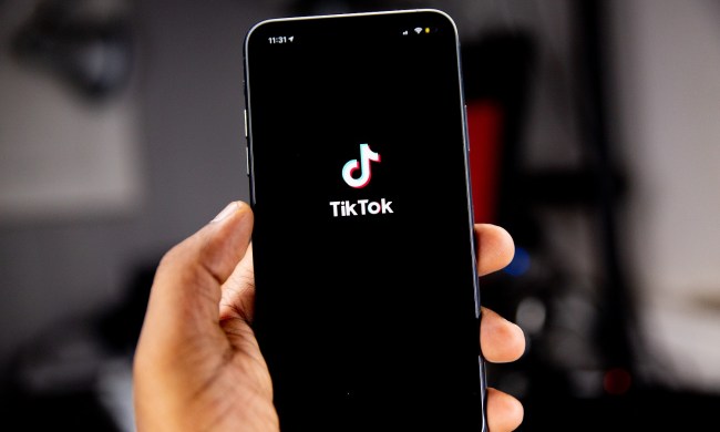 Person's hand holding a smartphone with TikTok's logo on screen, all in front of a blurred background.