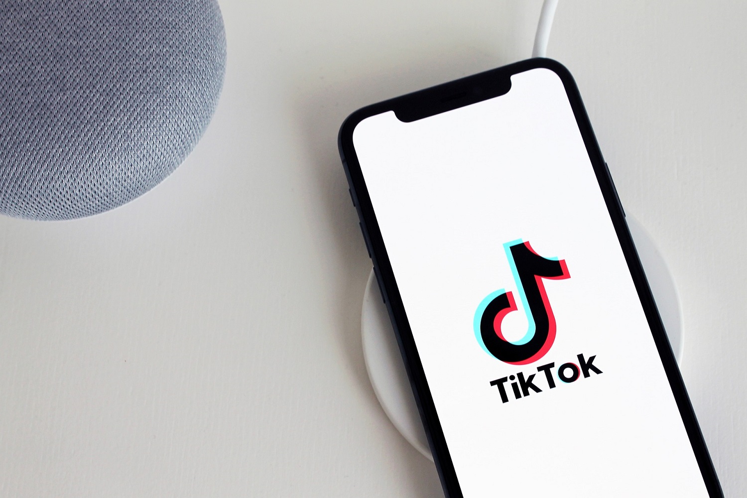 Um smartphone e dois outros dispositivos em uma mesa branca.  O smartphone tem o logotipo do TikTok na tela.