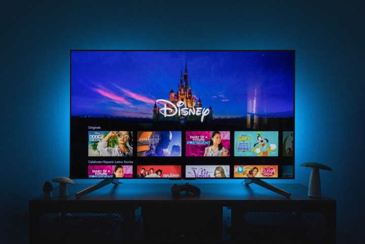 La aplicación Disney+ en la pantalla de un televisor mientras luces azules iluminan la pared de atrás.