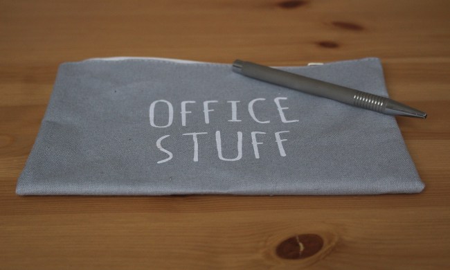 A gray cloth bag that has the words "Office Stuff" emblazoned on it, resting on a wooden table. There is also a pen on top of the bag.