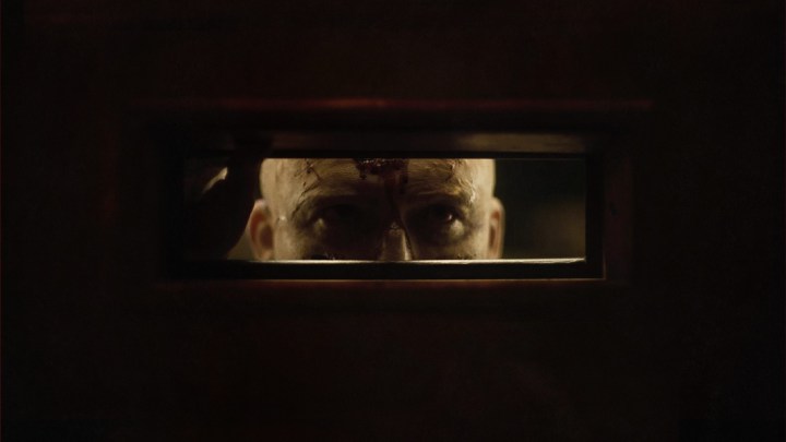 O personagem de Rory Kinnear olha através da caixa de correio de uma porta em uma cena de Homens.