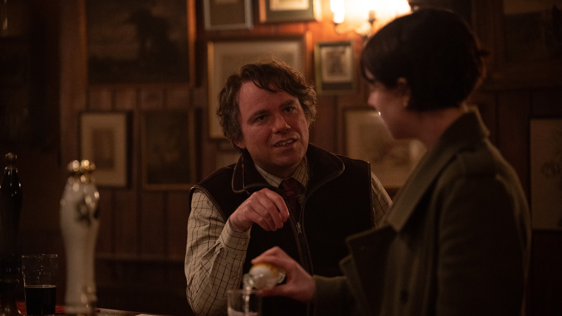Rory Kinnear, como Geoffrey, fala com a personagem de Jessie Buckley em um pub em uma cena de Homens.