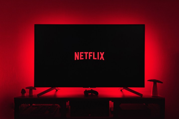 لوگوی نتفلیکس روی صفحه تلویزیون ظاهر می شود در حالی که چراغ های قرمز دیوار پشت را روشن می کند.