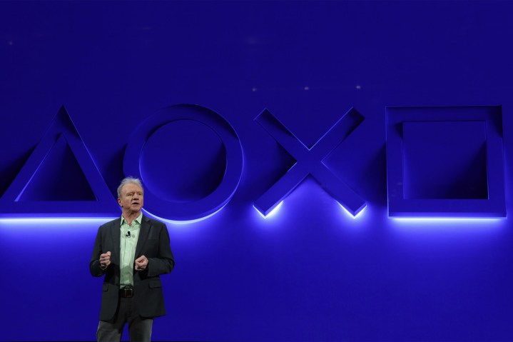 El CEO y presidente de Playstation, Jim Ryan, se encuentra frente a una pared azul con los símbolos de los botones de Playstation iluminados.