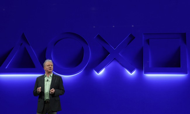 Playstation CEO and president, Jim Ryan, stands in front of a blue wall with Playstation button symbols illuminated.