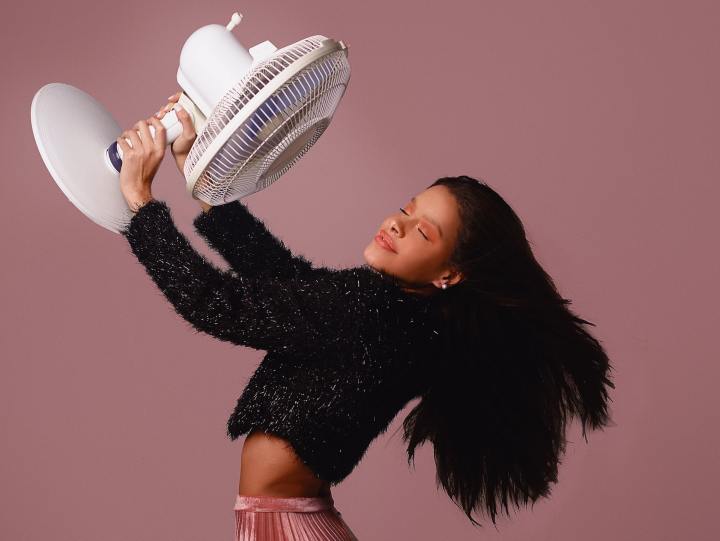 A woman holds a fan up in front of her to cool off. 