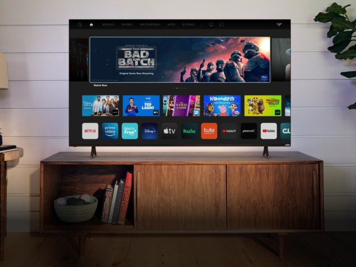 Vizio 55-inch 4K TV displaying its home screen while placed on a TV stand.