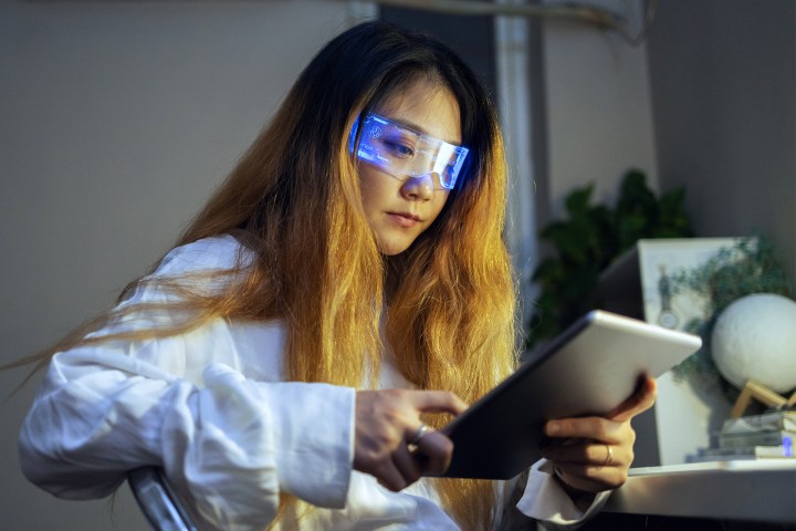 Woman wearing augmented reality glasses checking her digital tablet.
