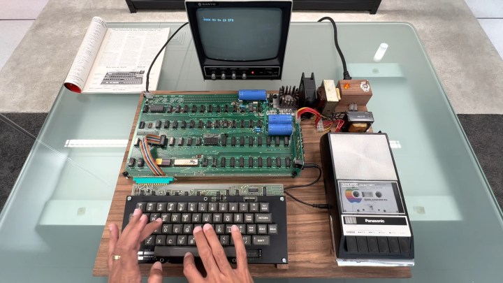 Apple-1 computer, sat on a table, with a person typing on its keyboard.
